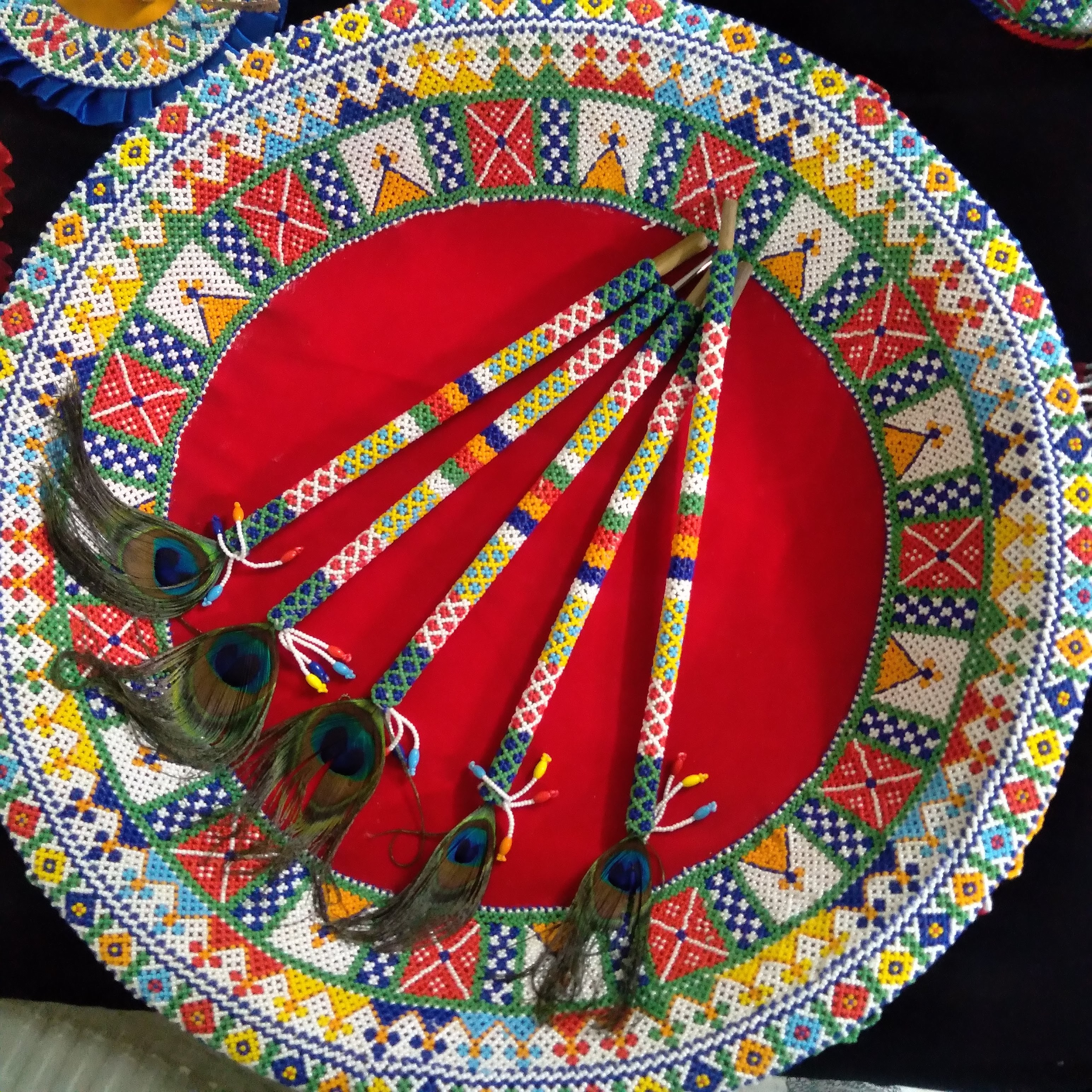 Set of five colourful beaded dandiya sticks with peacock feathers arranged on a round beaded mat